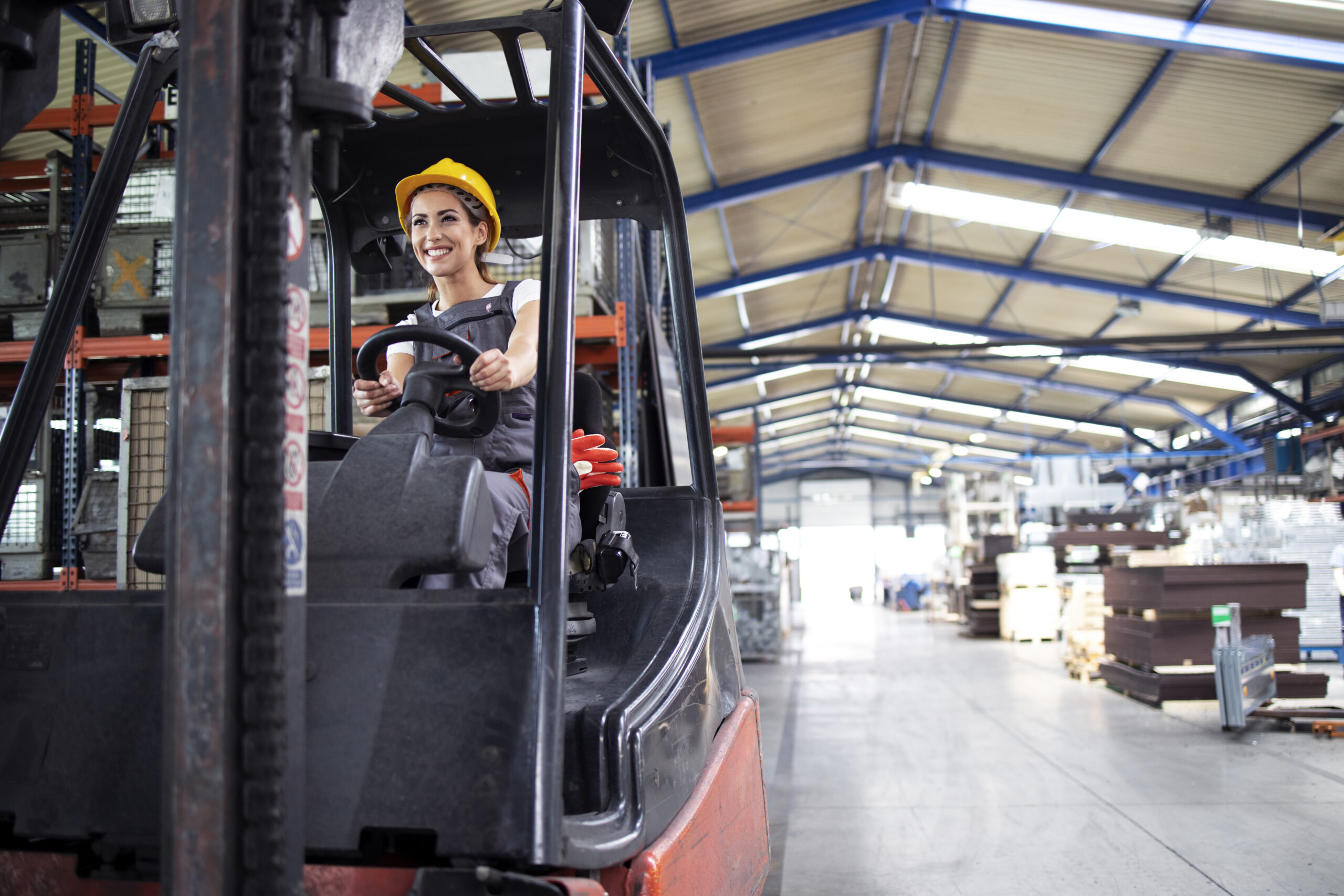Professional female industrial driver operating forklift machine in factory's hall.